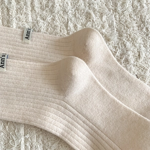 Macro detail of beige ribbed wool knee socks featuring a minimalist stitched Ann's fabric label