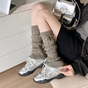 Close-up of grey cable-knit leg warmers featuring fluffy pom-poms and ribbed textures