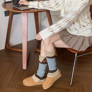 Detail of striped knitted leg warmer sleeves on camel suede boots in a cozy indoor setting