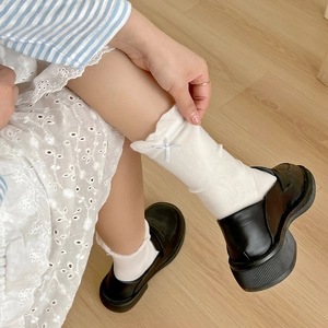 White knit mid-calf socks with ruffle trim and bow accents, paired with black loafers
