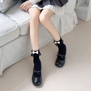 Detail von schwarzen Mary Jane Schuhen und Socken mit Spitzenbesatz und weißer Schleife