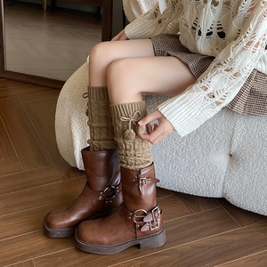 Detail of cable knit leg warmers with fluffy pom-poms over brown buckle boots