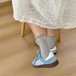 Detail of light grey knit socks with frilled edges and a delicate white bow accent