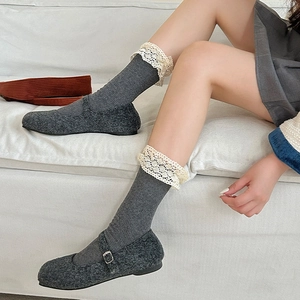 Detail of dark grey Mary Jane shoes with vintage lace trim socks on light grey sofa