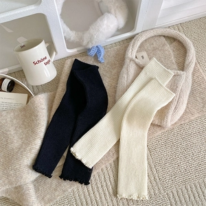 Close-up of knit leg warmers with vertical ribs and delicate ruffled edge detail