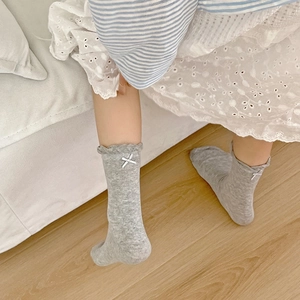Detail of grey crew socks with ruffle cuffs and white ribbon bows on kids feet