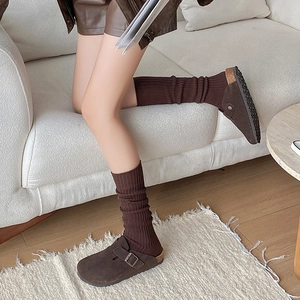 Close-up of brown suede clogs styled with ribbed knit calf socks on a textured carpet