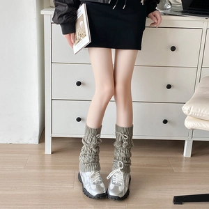 Close-up of olive green cable knit leg warmers with pom-poms and bow detail