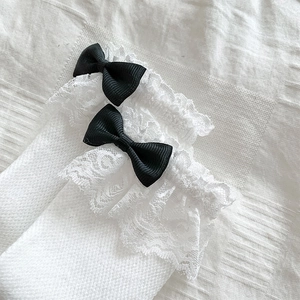Detailansicht weißer Socken mit Spitzenbesatz und eleganten schwarzen Schleifen