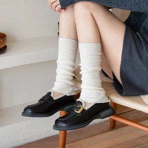 Detail of white ribbed knit leg warmers paired with black fleece-lined loafers and gold buckle