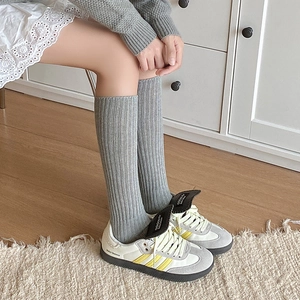 Close-up of grey ribbed knit long socks worn with stylish leather sneakers on a rug