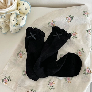 Detail of black frilly crew socks featuring delicate lace edges and silk ribbon bows
