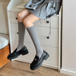 Close-up of grey ribbed wool knee-high socks paired with black platform loafers