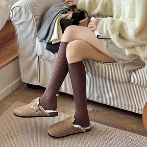 Detail of dark brown ribbed wool socks with white logo patch and cozy fleece mules