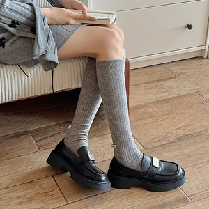 Detail of grey ribbed wool socks with small white label paired with black platform loafers