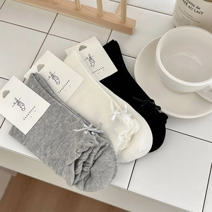 Close-up of ruffled cuffs and bow details on cotton crew socks in grey, white and black