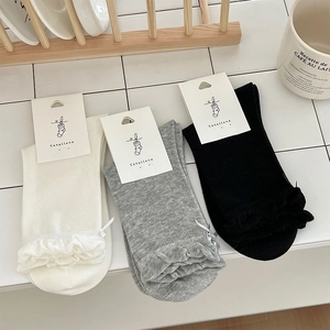 Detail of three pairs of cotton mid-calf socks with ruffle trim and tiny bows in soft light
