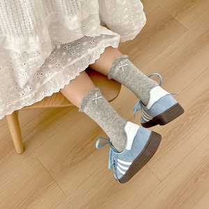 Grey frilly crew socks with bow embroidery paired with blue suede sneakers on wood floor