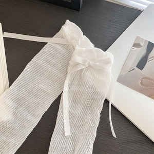 Detailed close-up of white mesh leg warmers with ribbon bows on dark wood background