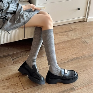 Thick grey ribbed wool knee-high socks paired with stylish black platform loafers