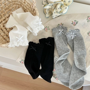 Three pairs of knit baby socks with ruffles and bows in white, black, and grey colors