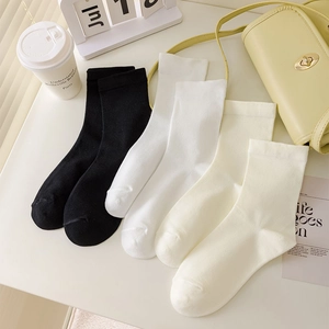 Close-up of basic solid-colored mid-calf socks in black, white and beige on white desk