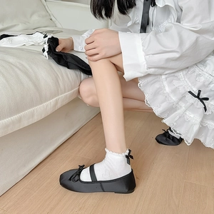 Close-up of black satin ballet flats with white lace trim socks and ribbon bows