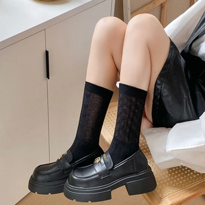 Detail of black platform loafers with gold logo buckle and crew socks worn by a model