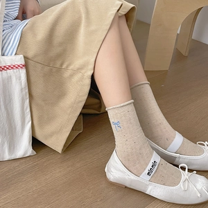 Detail of oat-colored crew socks featuring blue bow embroidery and rolled cuffs