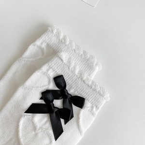 Detail of white knit heart texture socks with black ribbon bows and scalloped edges