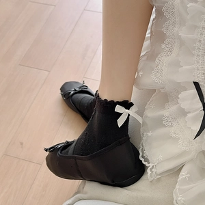 Detail of black frilly socks with white satin bows paired with black ballet flats
