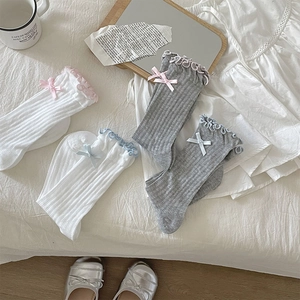 Detail of girls cotton rib knit socks with ruffled edges and ribbon bows in soft white and grey