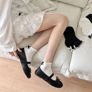 Detail of white ruffle socks with bows and heart patterns worn with black ballet flats