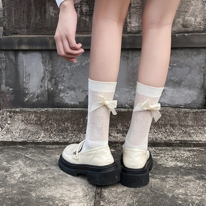 Détail de chaussettes mi-mollet blanc cassé avec nœuds en satin et mocassins à plateforme
