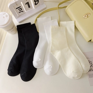Three pairs of cotton crew socks in black, white, and beige on a stylish desk setting
