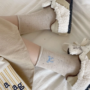 Close-up of beige crew socks with blue bow embroidery and vertical ribbed texture