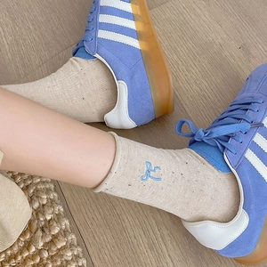 Close-up of beige knit socks with blue bow embroidery paired with blue suede sneakers