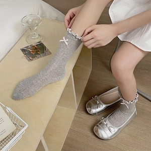 Detail of grey socks with white ruffled edges and pink bows paired with silver ballet flats