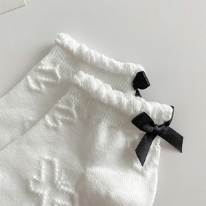 Detail of white cotton blend socks with jacquard texture and black satin bow accent