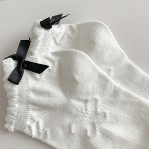Detail of white cotton socks with black silk bows and embossed cross knit texture