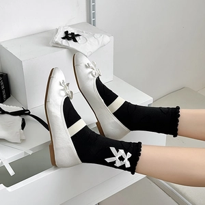 Detail of balletcore style black socks with white bows and white satin flats