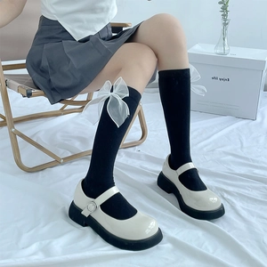Detail of black knee-high socks with white tulle bows and Mary Jane shoes