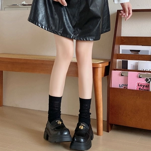 Detail of black platform loafers with gold metal logo and mesh crew socks on a model