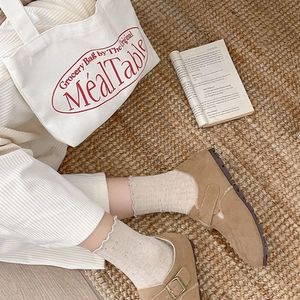 Close-up of brown Mary Jane shoes with beige ruffled crew socks on a woven rug