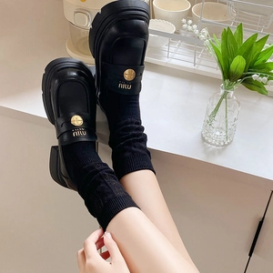 Detail of black platform loafers with gold logo buckle and mesh crew socks