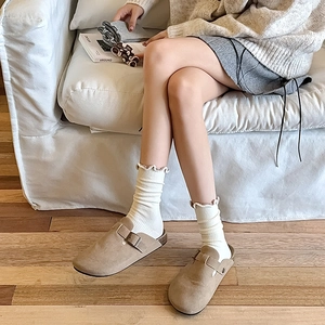 Close-up of khaki suede clogs with adjustable metal buckle and beige ruffled knit socks