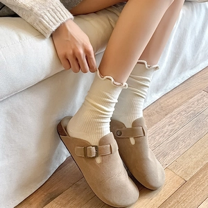Detail of khaki suede mules with metal buckle and ruffled white crew socks on wood floor