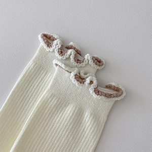 Macro shot of cream white crew socks featuring lettuce edge trim and brown piping detail