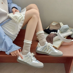 Detail of beige crew socks with lace ruffled trim paired with silver leather trainers