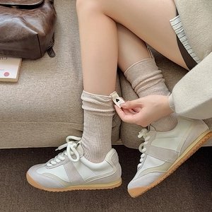 Dettaglio di calze beige in maglia a coste con toppa a cuore e sneakers stile vintage